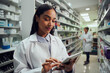 © StratfordProductions - Smiling young female worker in pharmacy wearing labcoat checking inventory using digital tablet