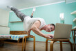 A muscular man keeps balance on one hand and works at a laptop during covid-19. Self-isolation, teleworking and home fitness concept