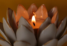 Macro Detail Shot With Wide Depth Of Field Of Candle Wick With Flame In A Lotus Flower Candle Holder On A Deep Yellow Background