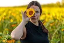 Young Beautiful Girl In A Field Of Sunflowers, Closes Her Eyes With A Flower. Close-up Portrait