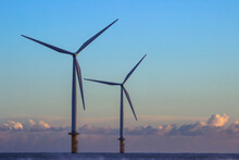 Two Off Shore Wind Turbines Operating In Calm Conditions With Dramatic Sky In The Distance