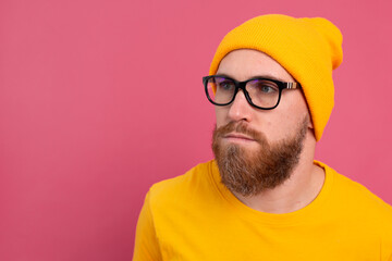 Portrait of stylish handsome  european bearded man in casual yellow shirt hat and glasses on pink background