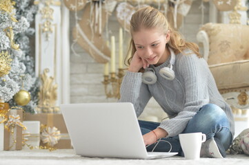 Beautiful girl with laptop sitting on floor near Christmas tree