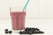 Blueberry smoothie in a glass jar mug with straw. With fruits on a white table.