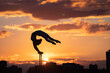 Flexible female circus Artist keep balance and doing contortion on the rooftop against dramatic sunset and cityscape. Motivation, passion and achievement concept 