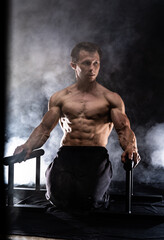 Muscular build man doing crossfit on parallels bar indoor on black, smoked background. concept of healthy lifestyle and calisthenic