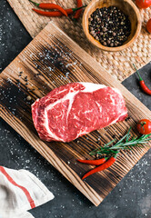 Wall Mural - Raw rib eye beef steak on wooden board with chili pepper, salt and rosemary, top view.