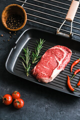 Wall Mural - Raw rib eye beef steak on black grilling pan with chili pepper and rosemary, top view.