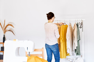 Woman takes linen dress on hanger from clothes rack. Slow Fashion. Conscious consumption. Crisis in the fashion industry, retail. Eco-friendly, Sustainable seasonal Sale concept. Zero waste.