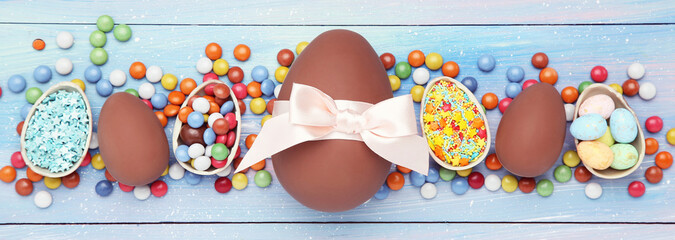 Wall Mural - Easter chocolate eggs with candies and sprinkles on blue wooden table