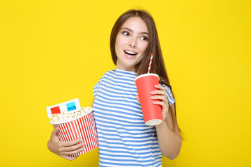 Beautiful girl holding bucket of popcorn and drink on yellow background