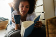 © lordn - Pretty african american young woman reading a book at home at her cozy corner