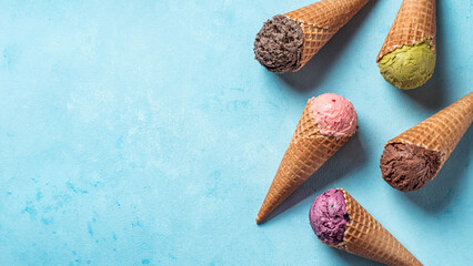 Various ice cream scoops in cones with copy space. Colorful ice cream in cones chocolate, strawberry, blueberry, pistachio or matcha, biscuits chocolate sandwich cookies on blue background. Top view