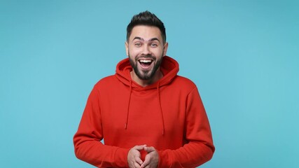 Wall Mural - Excited surprised bearded young man 20s years old in casual red streetwear hoodie isolated on pastel blue color background in studio. People lifestyle concept. Say wow covering mouth put hands on head