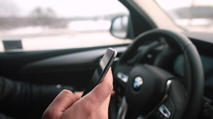 Poster - The man's hand uses the phone in his hand while driving a car. Communication while driving on the road. Use of mobile internet. Driver multitasking.