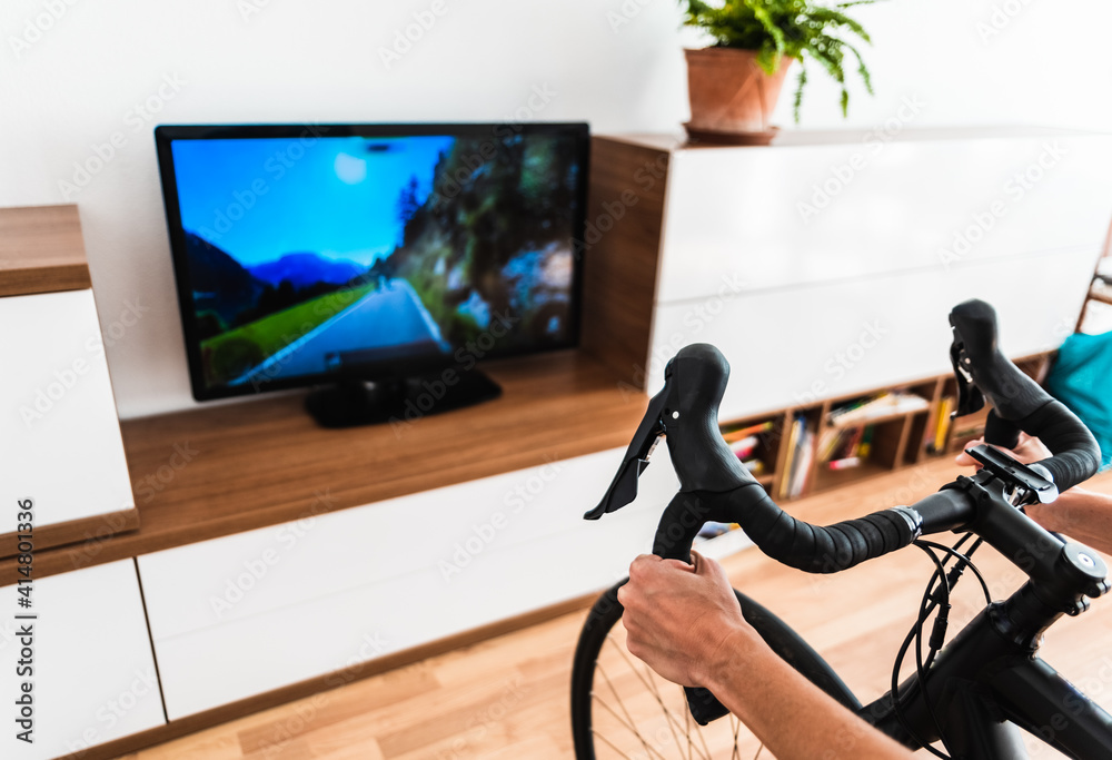 Cycling Indoor with exercise bike trainer motivating himself with the gamification of sport. - obrazy, fototapety, plakaty 