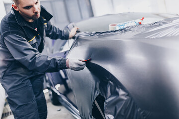 Car wrapping specialist putting vinyl foil or film on car. Selective focus.