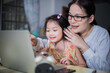 © sticker2you - Asian woman teaching her duagther with laptop and smartphone study online concept.