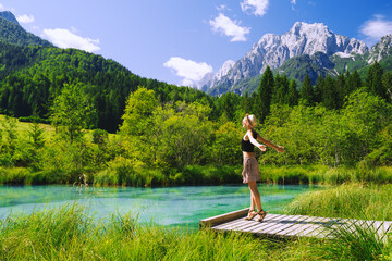 People in nature. Tourist woman with raised arms up in green nature background. View on Zelenci (into English means - green) natural reserve in Slovenia, Europe. Travel, Freedom, Lifestyle concept.