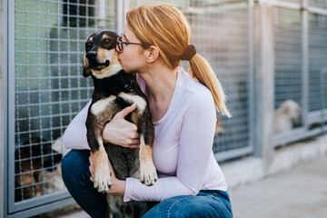 Young adult woman holding adorable dog in animal shelter.