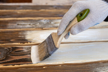 Painting a wooden background with white paint. Hand with brush