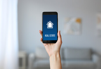 young woman with mobile phone using real estate website at home