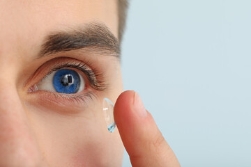 Young man putting in contact lenses on color background, closeup