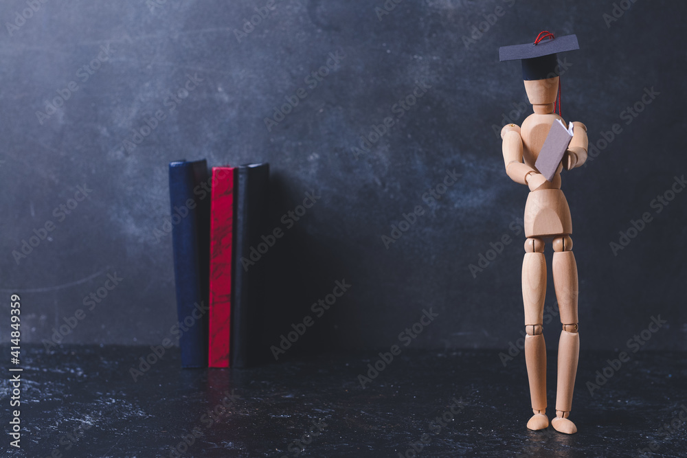 Wooden mannequin in graduation hat on dark background