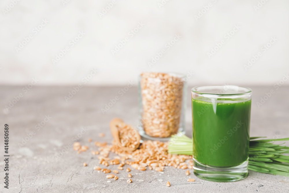 Glass with fresh wheatgrass juice and seeds on gray background