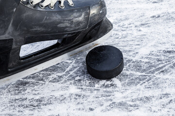 Wall Mural - Old black hockey male skate and rubber puck on ice background. Closeup.