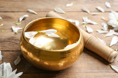 Obraz Dibond Golden singing bowl with petals and mallet on wooden table, closeup. Sound healing
