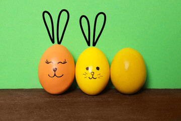 Two eggs with drawn faces and ears as Easter bunnies among others on wooden table against green background