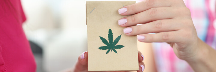 Wall Mural - Female hands hold package with hemp leaves close-up. Legal delivery of marijuana narcotic substances concept.