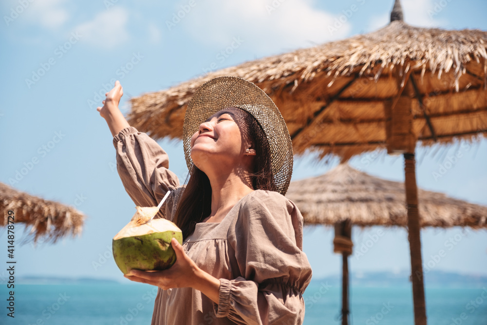 Portrait image of a beautiful asian woman holding a fresh coconut and enjoying on the beach - obrazy, fototapety, plakaty 