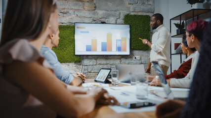 Office Conference Room Meeting: Black Chief Company Strategist Doing TV Presentation to a Diverse Team of Multi-Ethnic Professional Businesspeople, Explaining Marketing Strategy, Data Analysis