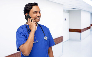 Sticker - healthcare, profession and medicine concept - happy smiling indian doctor or male nurse in blue uniform with stethoscope calling on smartphone over corridor at hospital on background