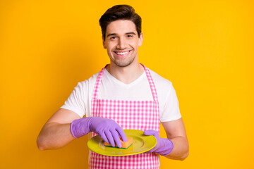 Wall Mural - Photo portrait of man in rubber gloves washing dishes with sponge isolated on vivid yellow colored background