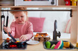 cute toddler baby girl playing on toy kitchen at home, pretends frying eggs