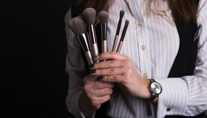 Girl make-up artist holds brushes for visage. Close-up photo in studio on black background