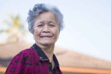 Senior woman with short gray hair smiling and looking at the camera while standing outdoors. Space for text. Concept of aged people and healthcare