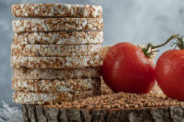 Stack of tasty rice cakes, tomatoes and raw buckwheat on wooden piece