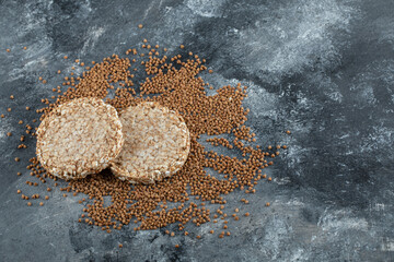 Two crispbread and uncooked buckwheat on marble surface