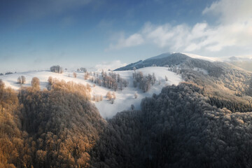 Amazing aerial view of mountains range, meadows and snow-capped peaks in winter time. Forest with frost glowing with bright warm sunrise light