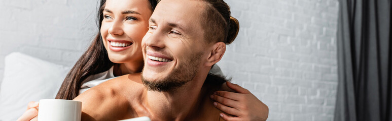 Smiling woman with cup hugging boyfriend at home, banner