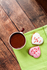 a cup of hot chocolate and two heart-shaped gingerbreads on a green towel on brown wooden background