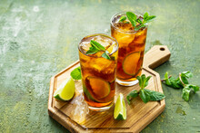 Refreshing Drink, Iced Tea With Lime Wedges In Glasses On A Wooden Board On A Green Concrete Background. Summer Drinks.
