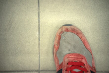 An Old Ragged Red Running Shoe On The Tiled Floor