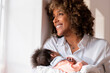 © steve brookland/Westend61 - Happy mother with newborn baby looking away while standing by window at home