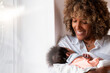 © steve brookland/Westend61 - Smiling woman holding newborn baby while standing at home