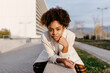 © Tania Cervi√°n/Westend61 - Confident young woman with afro hair sitting on retaining wall in city